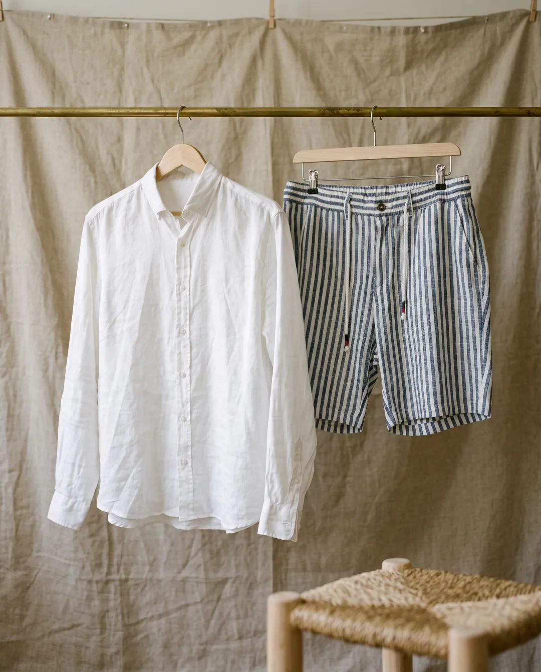 White linen shirt and striped shorts hanging on a brass rail