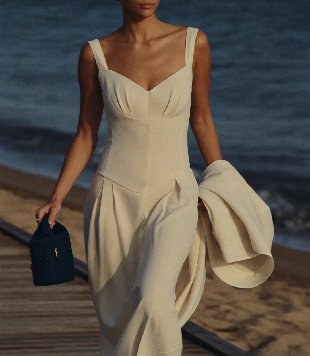 Woman in a flowing cream linen summer dress on a beach promenade